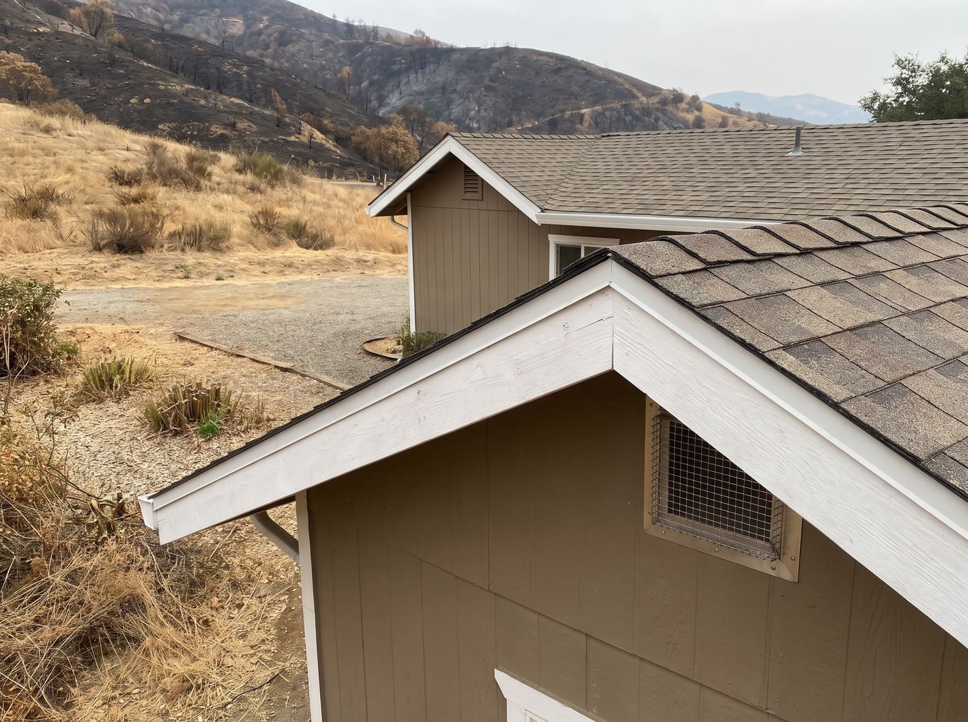 An ember-resistant eave vent on a foothill house with burned slopes behind
