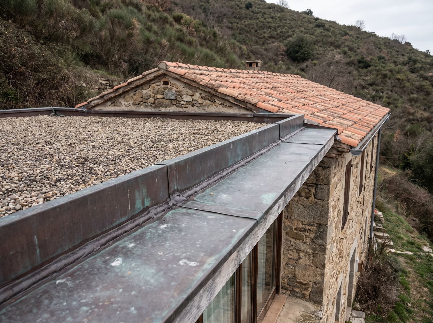 Metal transition flashing where a flat roof section meets a pitched tile roof