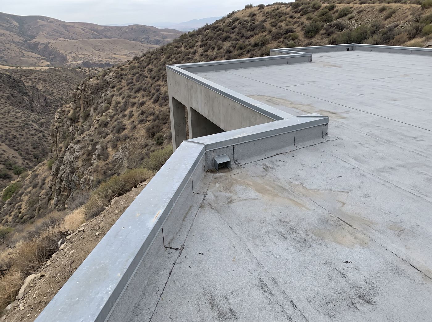 A flat roof deck on a canyon house with a parapet, metal coping and a scupper drain