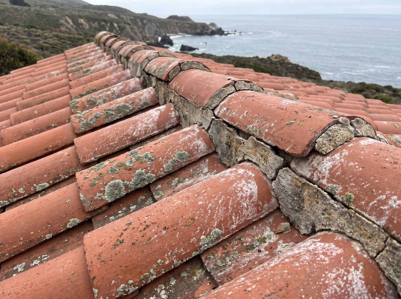 Weathered red clay barrel tiles with cracked mortar lifting at the ridge