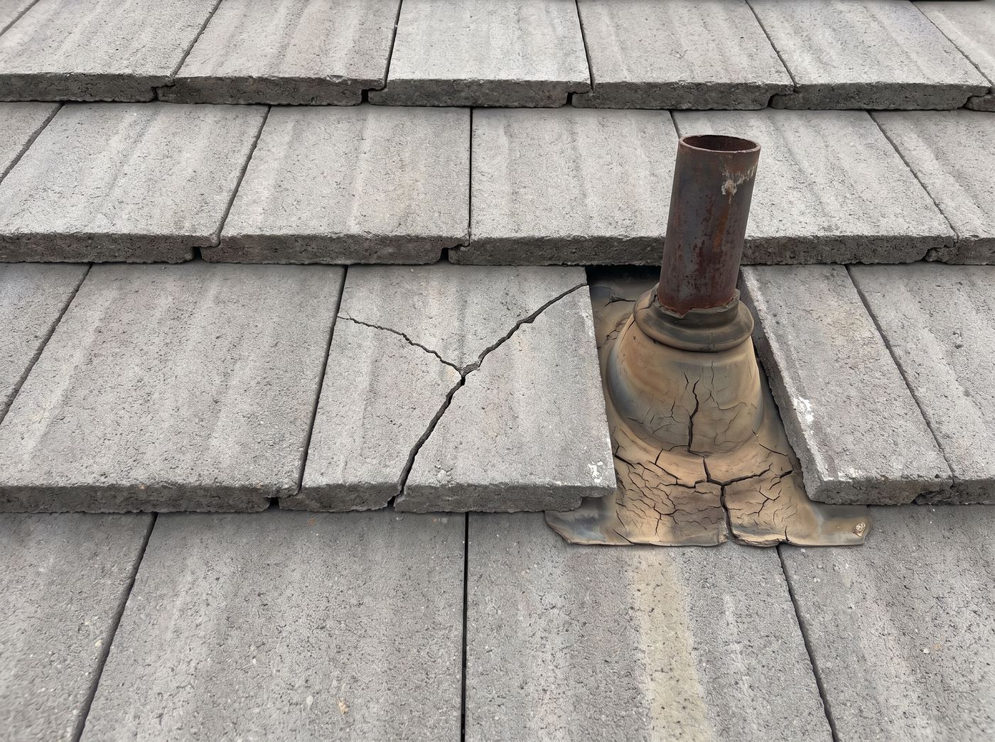 Concrete roof tiles with a cracked tile in the field and a cracked rubber vent boot