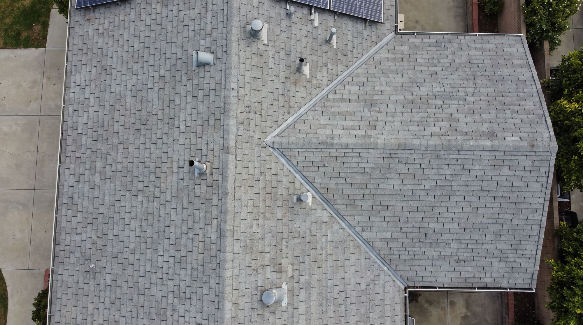 Overhead view of a suburban roof showing shingle courses, ridge, valley and vent pipes