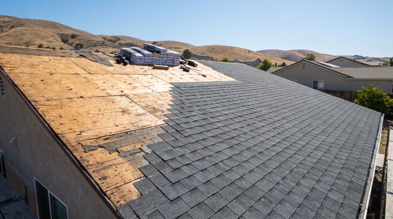 A roof part stripped to the deck and part covered in new shingles
